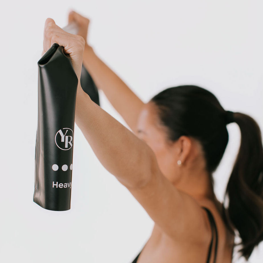 Black Heavy Stretch Resistance Band held overhead in Pilates movement - Detail | Your Reformer
